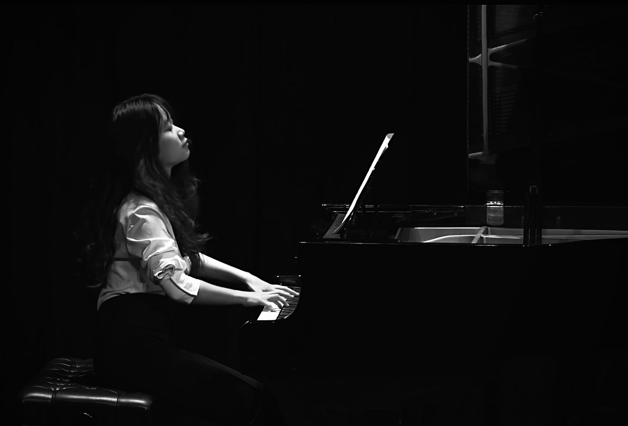 Ms Van performing at a grand piano under stage lights, photographed in black and white
