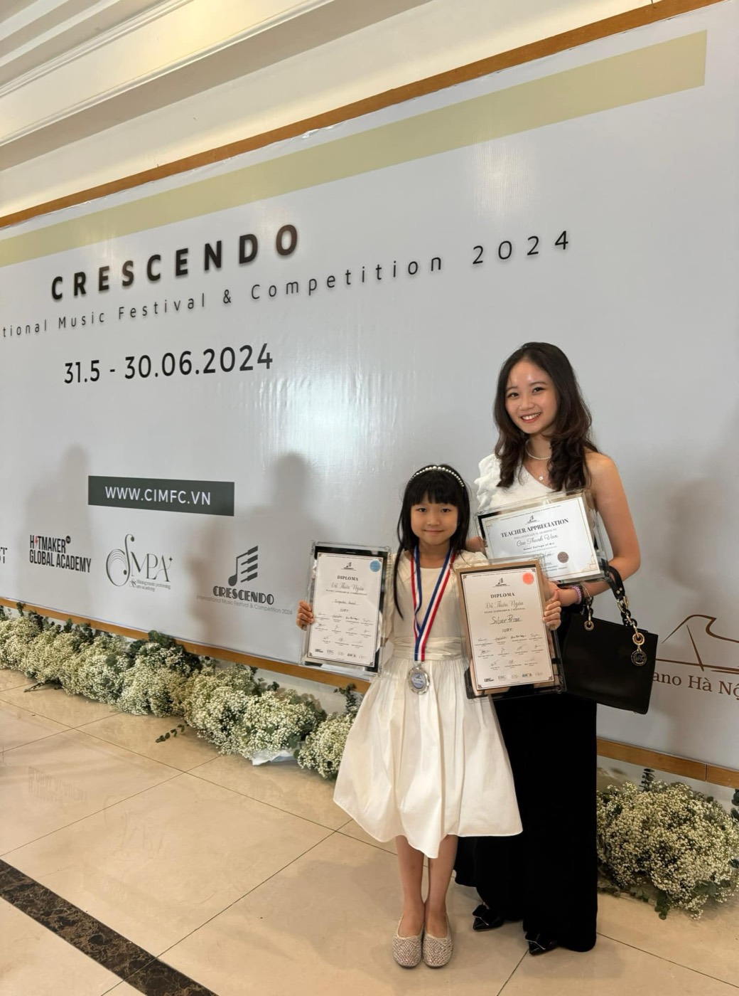 Ms Van smiling with her student, who holds Silver Prize and Perspective Prize diplomas, at Crescendo International 2024